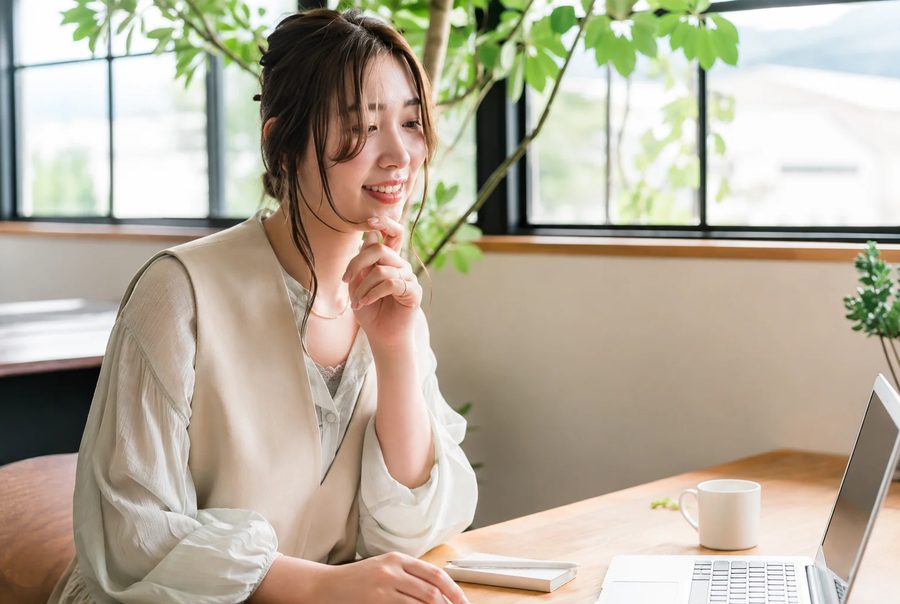窓辺の机でノートパソコンを開き、笑顔で学習する女性